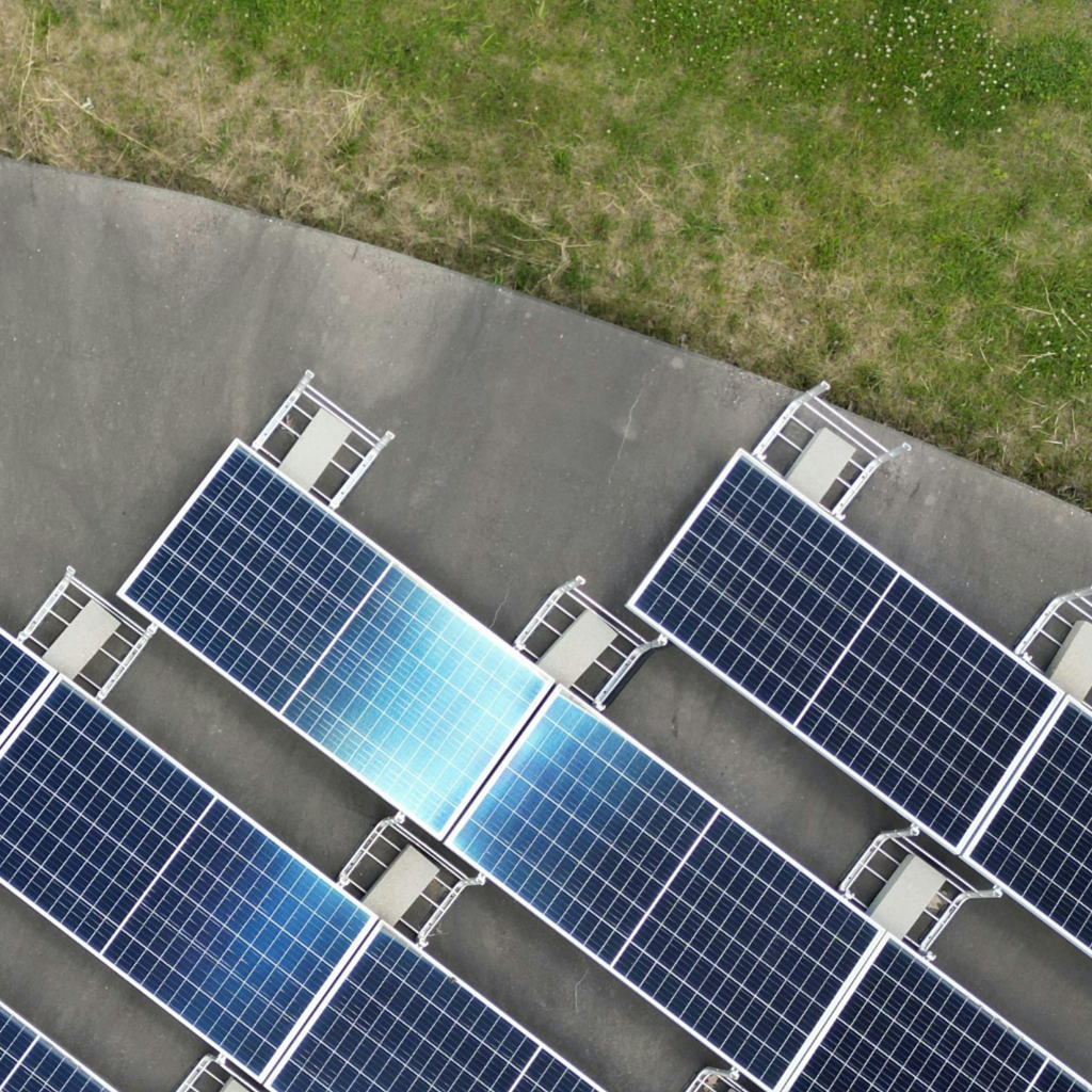 Rectangular solar panels on a concrete base with a grass patch to one side viewed from directly above.